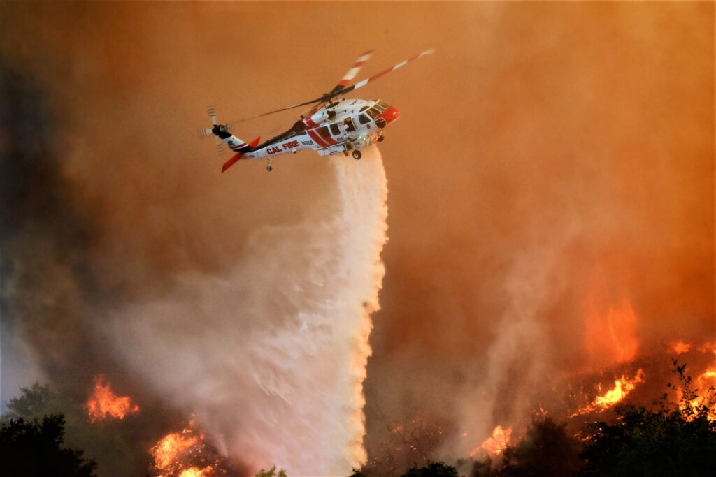 A CAL FIRE helicopter drops water on a wildfire. 